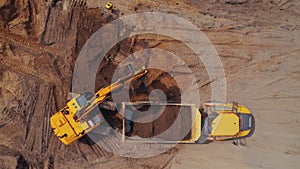 Yellow power shovel and construction track working on a sandy field. Building site concept.