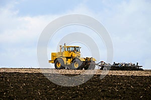 Yellow powerful wheeled tractor pulls the disc harrow