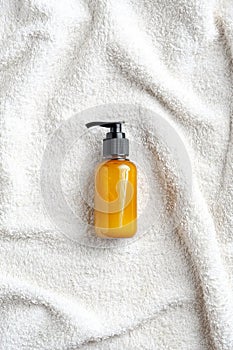 Yellow pump cosmetic bottle on white towel top in bathroom, top view.