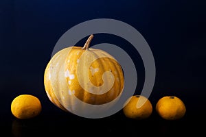 Yellow pumpkin and oranges on dark background. Fresh vegetables and fruits on black.