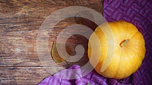 Yellow pumpkin, warm woolen scarf and autumn leaves on a wooden background.