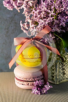 Yellow and purple French macaroons tied with a ribbon on the table, lilac in a vase.