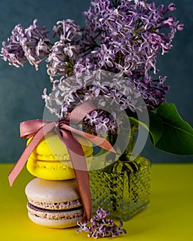 Yellow and purple French macaroons tied with a ribbon on the table, lilac in a vase.