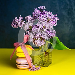 Yellow and purple French macaroons tied with a ribbon on the table, lilac in a vase.