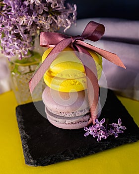 Yellow and purple French macaroons tied with a ribbon on the table, lilac in a vase.