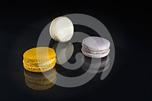 Yellow, purple and white macarons on black background with reflection