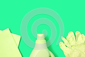 Yellow rag, plastic bottle and rubber gloves on green background. Cleaning concept