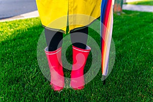 Yellow raincoat. Rubber pink boots against. Conceptual image of legs in boots on green grass