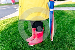 Yellow raincoat. Rubber pink boots against. Conceptual image of legs in boots on green grass