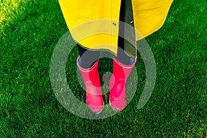 Yellow raincoat. Rubber pink boots against. Conceptual image of legs in boots on green grass