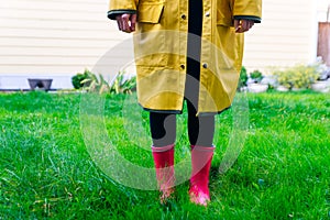 Yellow raincoat. Rubber pink boots against. Conceptual image of legs in boots on green grass