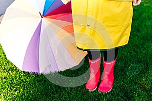 Yellow raincoat. Rubber pink boots against. Conceptual image of legs in boots on green grass. umbrella