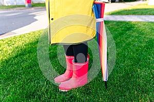 Yellow raincoat. Rubber pink boots against. Conceptual image of legs in boots on green grass. umbrella