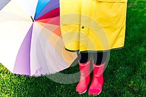 Yellow raincoat. Rubber pink boots against. Conceptual image of legs in boots on green grass. umbrella