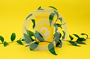 Yellow recycling bin embellished with fresh green leaves is set against yellow background