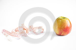 Yellow-red apple lies on a table with a measuring tape on a white