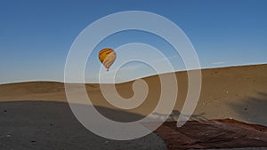 A yellow-red balloon is flying in a clear blue sky over the desert.