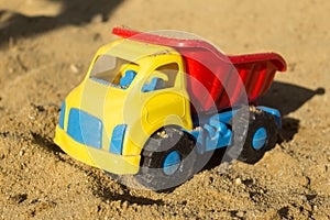 Yellow red and blue truck toy in sand, on the beach. Boy`s toys concept .