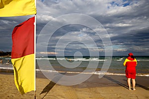 Yellow and red flags warning sign defocused female Volunteer lifesaving beach patrol standing watching tourists swimming flags