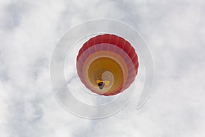 A yellow and red hot air balloon is seen from below in a sky filled with puffy white clouds