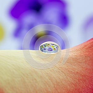 Yellow-red leaf of a rose and on it lies a small drop of water, in which the image of small purple pansy flowers is reflected.