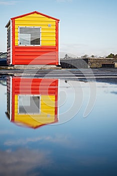 Yellow and red life guard station with sky reflection in a puddle of water. Rich blue cloudy sky. Low angle of view