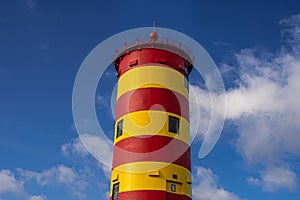 The yellow-red lighthouse of Pilsum with a blue cloudy sky