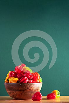 Yellow and red scotch bonnet chili peppers in wooden bowl over green background. Copy space.