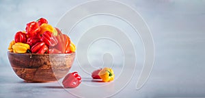 Yellow and red scotch bonnet chili peppers in wooden bowl over grey background. Copy space.