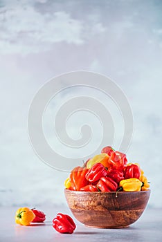 Yellow and red scotch bonnet chili peppers in wooden bowl over grey background. Copy space.