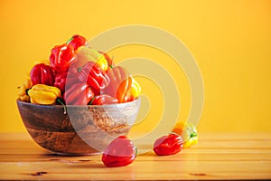 Yellow and red scotch bonnet chili peppers in wooden bowl over orange background. Copy space.