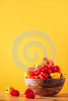 Yellow and red scotch bonnet chili peppers in wooden bowl over orange background. Copy space.