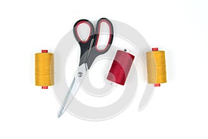 Yellow and red sewing thread coils with big black scissors on a white background