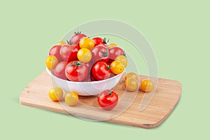 Yellow and red tomatoes in a plate on a cutting board. On a green background.