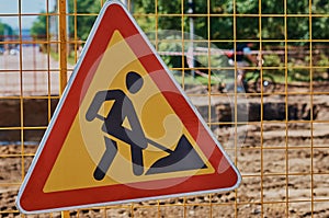 Yellow-red triangular road sign on a portable fence. Close up. Construction site. Road works. Sunny summer day