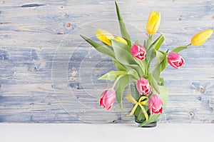 Yellow and red tulips in vase on blue shabby chic wood board. April spring background, home interior, decor.