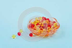 Yellow and red vitamin fat-soluble vitamins in glass plate on blue background. Variety of dietary supplements close up