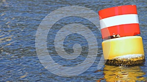 Yellow red and white steel navigational floating buoy in the blue Spree river water