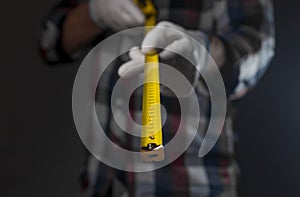 Yellow retractable tape measure tool in hands of man in shirt, closeup