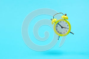 Yellow retro alarm clock levitates. Alarm clock in the old style on a blue background. 15-55 pm