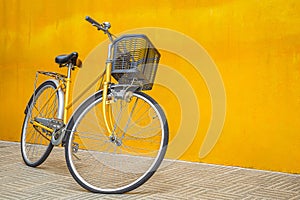 Yellow retro bicycle against a yellow wall. Vintage woman bike with a basket in front. Space for text
