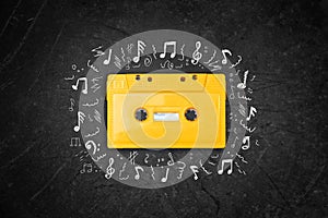 Yellow retro Cassette tape over blackboard. top view. music sketches