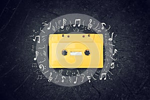 Yellow retro Cassette tape over blackboard. top view. music sketches.