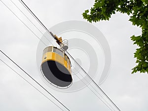 Yellow retro lift on a cable against the background of a cloudy sky and branches with green leaves