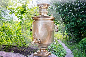 A yellow retro samovar boils water and releases smoke. A traditional Russian samovar is heated by wood in the garden