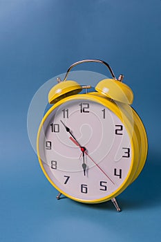 Yellow Retro style alarm clock with seven minutes to six o `clock