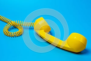 Yellow retro telephone receiver on blue background.