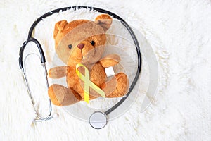 Yellow Ribbon on Bear doll with stethoscope on white background for supporting kid living and illness. September Childhood Cancer