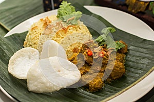 Yellow Rice with Rendang Beef and Shrimp Crackers, served on a banana leaf