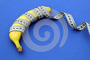 A yellow ripe banana with a centimeter flexible tape lies on a blue background.